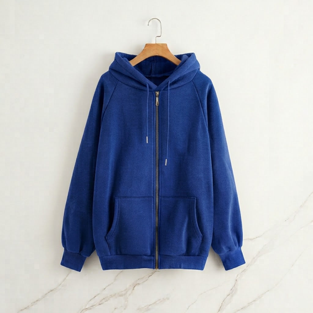 A royal blue zip-up hoodie with a drawstring hood and kangaroo pockets, hanging on a wooden hanger against a light off-white marble wall.