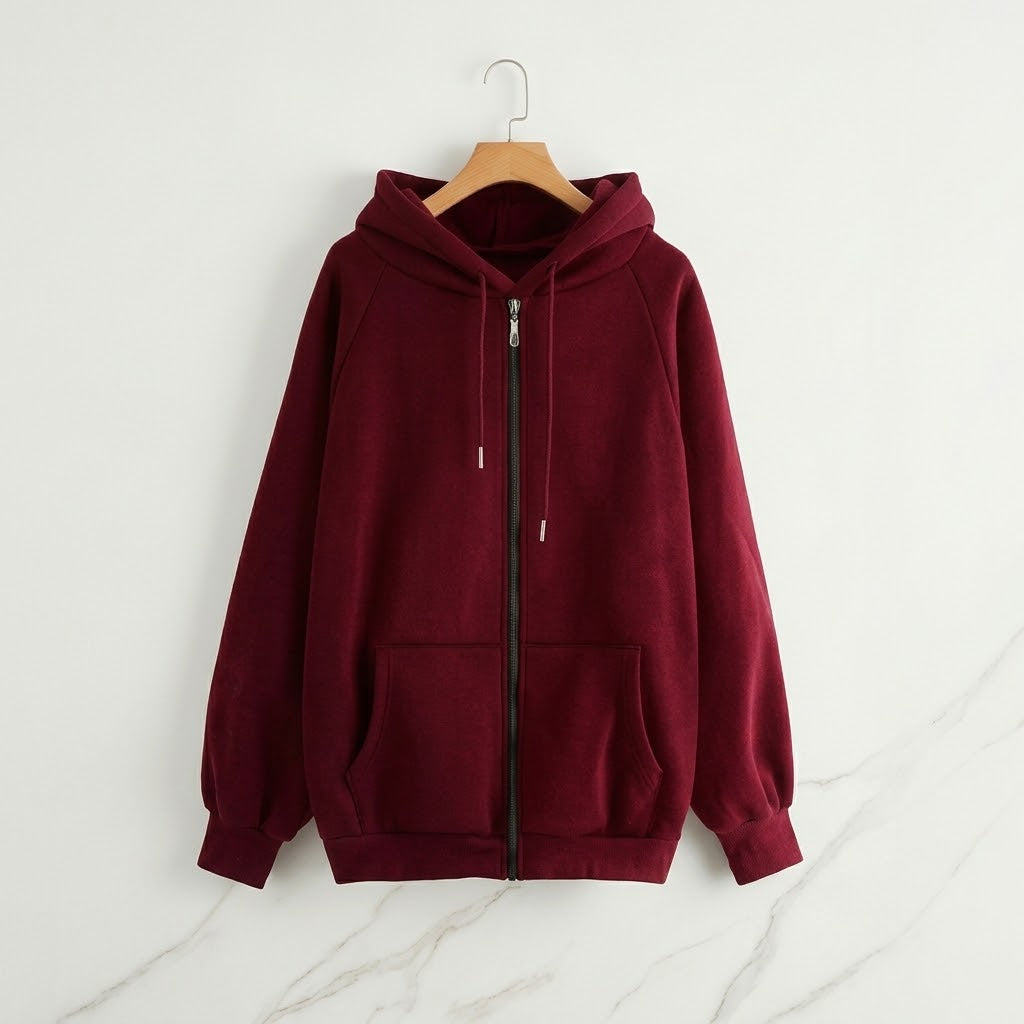 A burgundy zip-up hoodie with a drawstring hood and front pockets, hanging on a wooden hanger against a white wall with light gray marble veining.