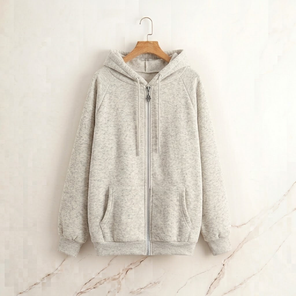 A light gray heather zip-up hoodie with a drawstring hood and kangaroo pockets, hanging on a wooden hanger against a light beige marble-textured wall.