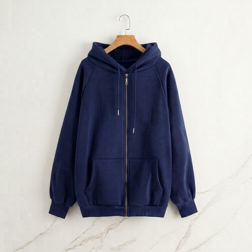 A navy blue zip-up hoodie with a drawstring hood and front kangaroo pockets, hanging on a wooden hanger against a light textured wall.